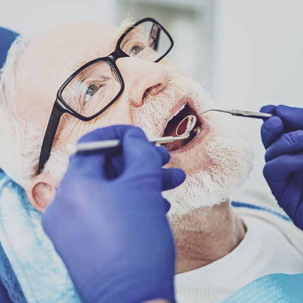 Portrait of Senior Man Wearing Glasses and Having his Crowns Checked by a Dentist at Ennis Family Dental