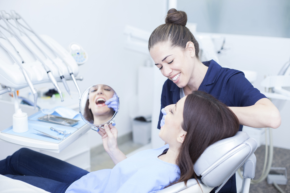 Female Adult Holding a Mirror while an Ennis Family Dental Dentist is Performing a Check Up on Her Teeth