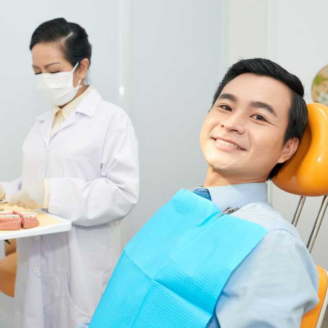 Portrait of Smiling Asian Man Sitting in an Orange Dentist Chair Awaiting Extraction by an Ennis Dental Family Dentist